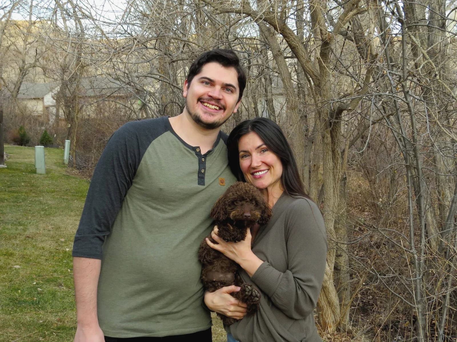 Anna and Brandon smiling outdoors, Anna holding their chocolate doodle puppy